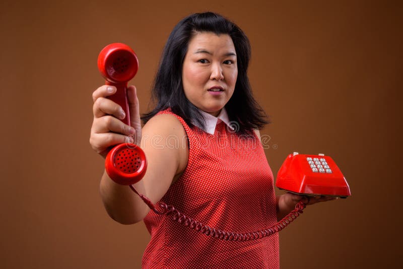 Mooie te zware Aziatische vrouw die oude rode telefoon geven stock foto Mooie te zware Aziatische vrouw die oude rode telefoon geven stock foto