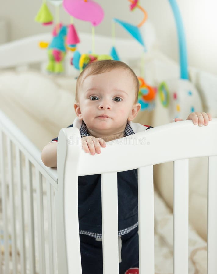 Mooie 9 van de babymaanden oud jongen die zich in voederbak bij slaapkamer bevinden royalty-vrije stock fotografie Mooie 9 van de babymaanden oud jongen die zich in voederbak bij slaapkamer bevinden royalty-vrije stock fotografie