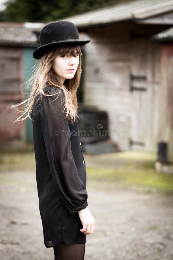 Portrait of a beautiful victorian style woman wearing a bowler hat and black dress standing in front of country farm stables. Portrait of a beautiful victorian style woman wearing a bowler hat and black dress standing in front of country farm stables