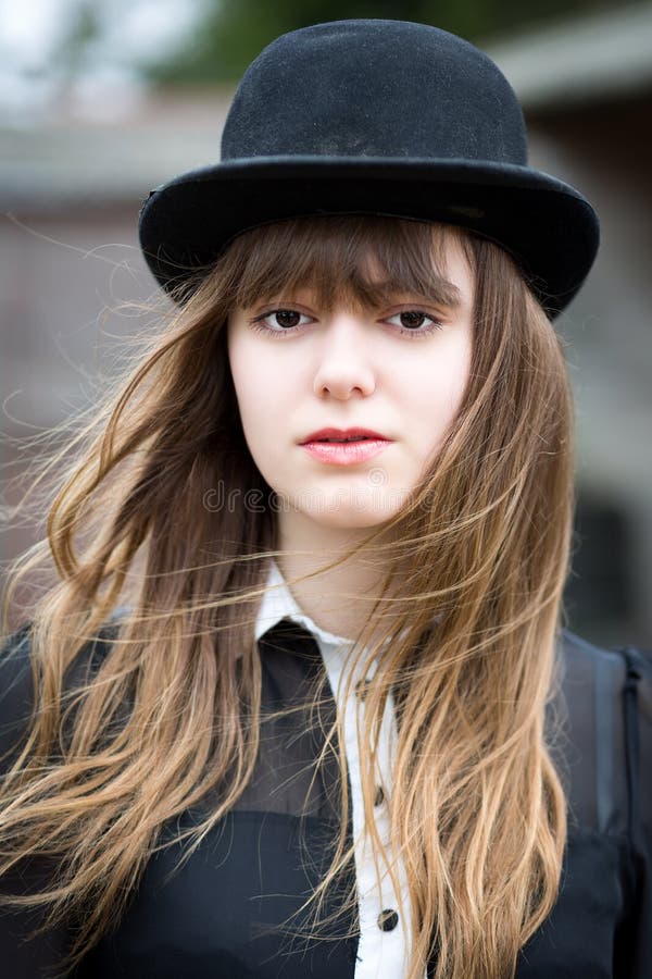 Portrait of a beautiful victorian style woman wearing a bowler hat and black dress standing in front of country farm stables. Portrait of a beautiful victorian style woman wearing a bowler hat and black dress standing in front of country farm stables