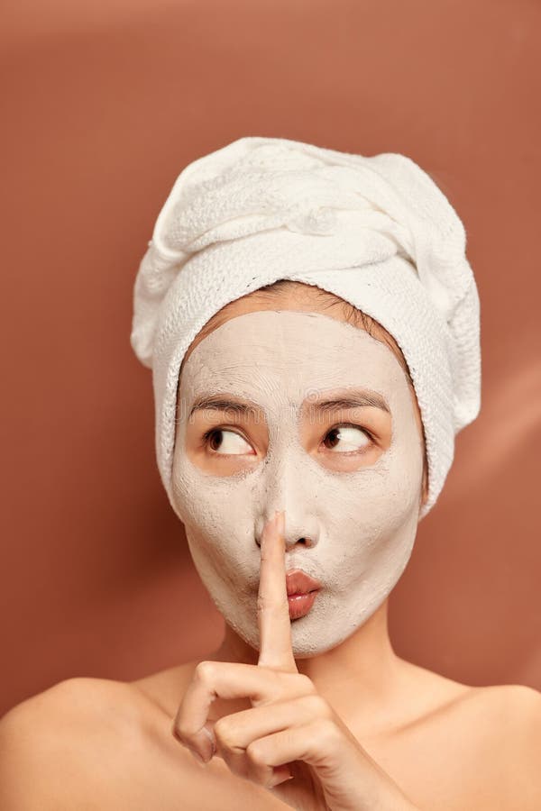 Beautiful woman with clay facial mask over orange background. Beauty treatment and spa concept. Beautiful woman with clay facial mask over orange background. Beauty treatment and spa concept.