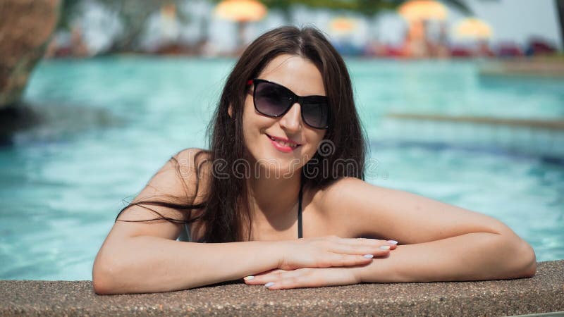 Mooie vrouw in zonnebril die in de pool stellen Het mooie meisje geniet de zomer van vakantie