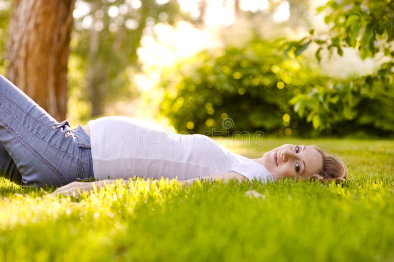 Mooie zwangere vrouw die op het gras in zonnige dag liggen stock fotografie Mooie zwangere vrouw die op het gras in zonnige dag liggen stock fotografie