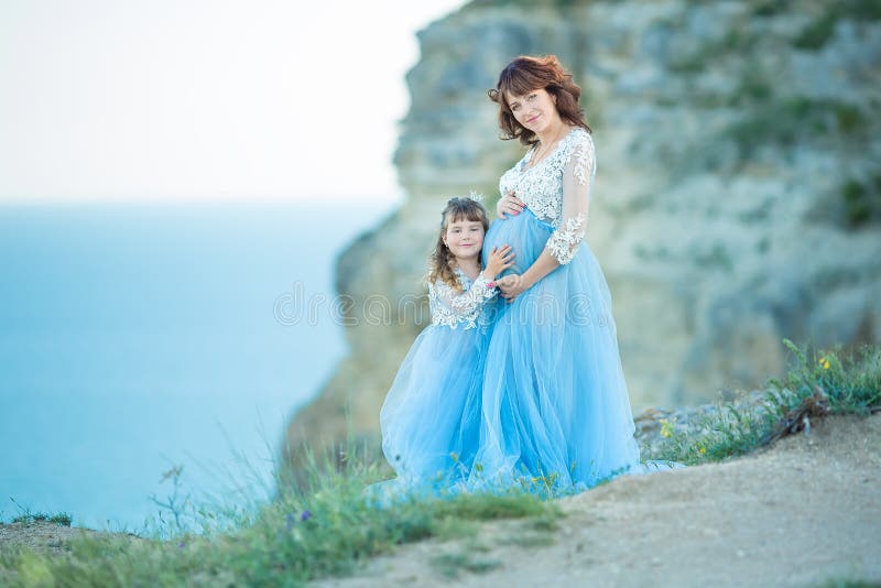 Mooie Zwangere Vrouw in romantische vliegende kleding op zee met binnen dochter dichtbij oude ruïnes van de stads Schitterend zwa stock fotografie Mooie Zwangere Vrouw in romantische vliegende kleding op zee met binnen dochter dichtbij oude ruïnes van de stads Schitterend zwa stock fotografie
