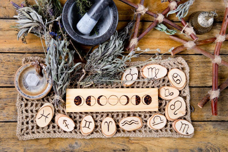 Moon Phases and astrological symbols with herb witch mortar and pestle, with branch pentagram and dried herb bundles on rustic wooden background