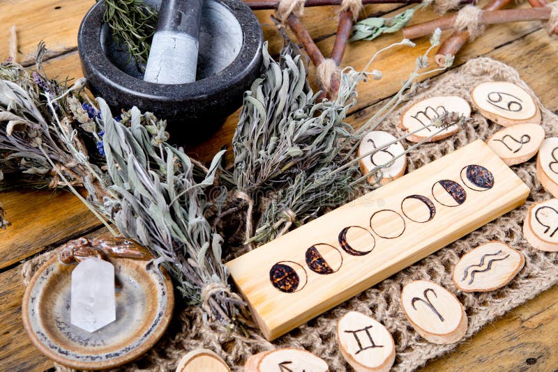 Moon Phases and astrological symbols with herb witch mortar and pestle, with branch pentagram and dried herb bundles on rustic wooden background