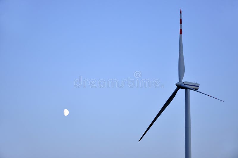 Moon and wind turbine against the blue sky