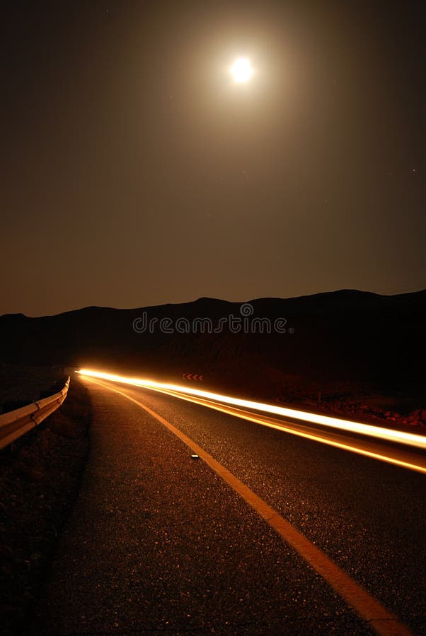 A moonlit road in a remote location late at night with car trails. A moonlit road in a remote location late at night with car trails