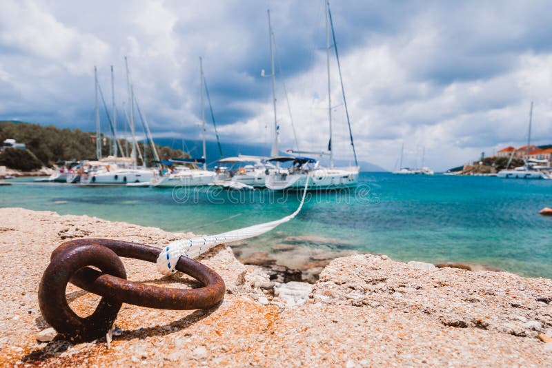 Mooring rope tied to rusty ring for rigging yachts in background. Wonderful view of port Fiskardo. Picturesque seascape