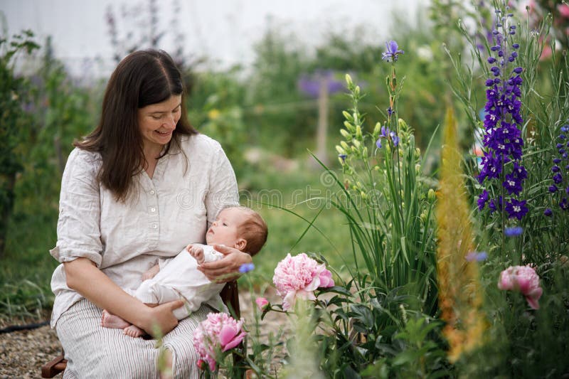 Mor kramar sött nyfött barn bland blommor i trädgården. Kärleksvård och familj på landsbygden. Grattis Mothers Day! royaltyfria bilder