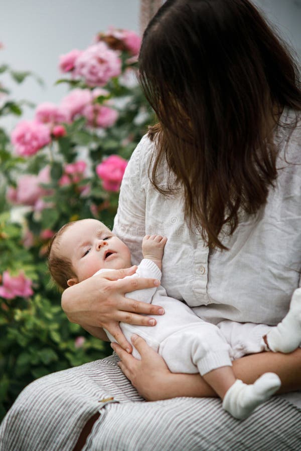 Mor kramar sött nyfött barn bland blommor i trädgården. Kärleksvård och familj på landsbygden. Grattis Mothers Day! royaltyfria foton