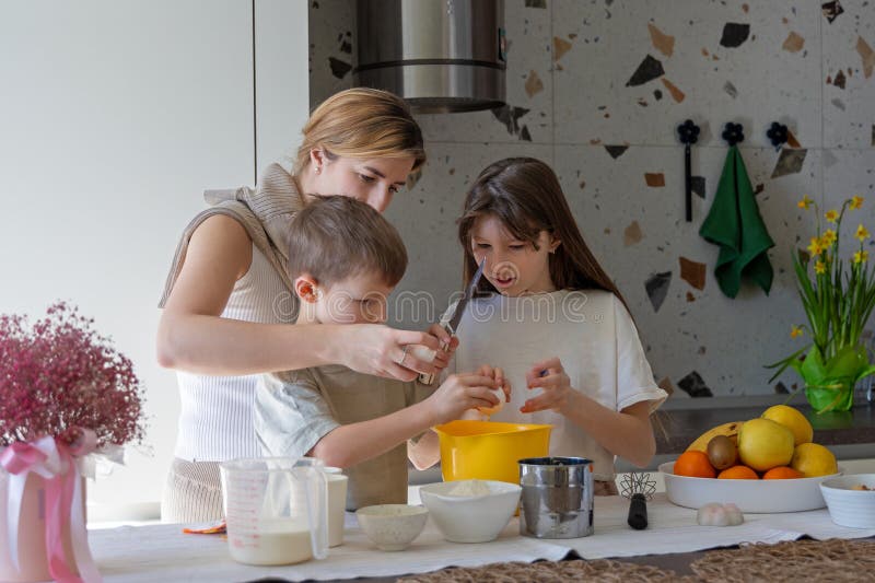 Mor och barn samlas i köket. Mor och två barn som krackar ägg och bereder ingredienser för gräddning arkivbild