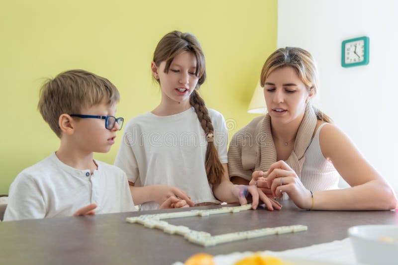 Mor och barn som spelar dominospel tillsammans. Ung mor och två barn som tillbringar kvalitet och spelar ett dominospel fotografering för bildbyråer