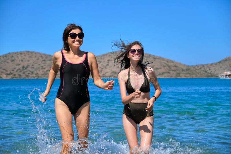 Mor och dotter tillsammans på stränder som rinner till havs i baddräkt royaltyfri fotografi