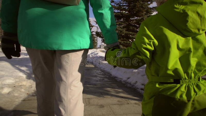 Mor och små barn som håller hand går längs sidpromenader med snöborrningar.