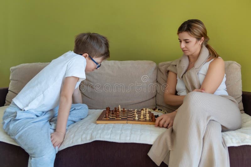 Mor och son fokuserade på schackspel. En ung pojke och hans mor sitter på en soffa och koncentrerar sig på en schackmatch som visa royaltyfria bilder