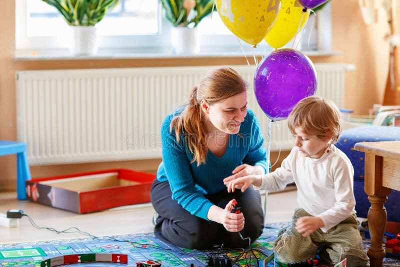 Mor och son leker med tävlingsbilar på racerbak inomhus med bilar. Glad liten förskolepojke och ung kvinna fotografering för bildbyråer