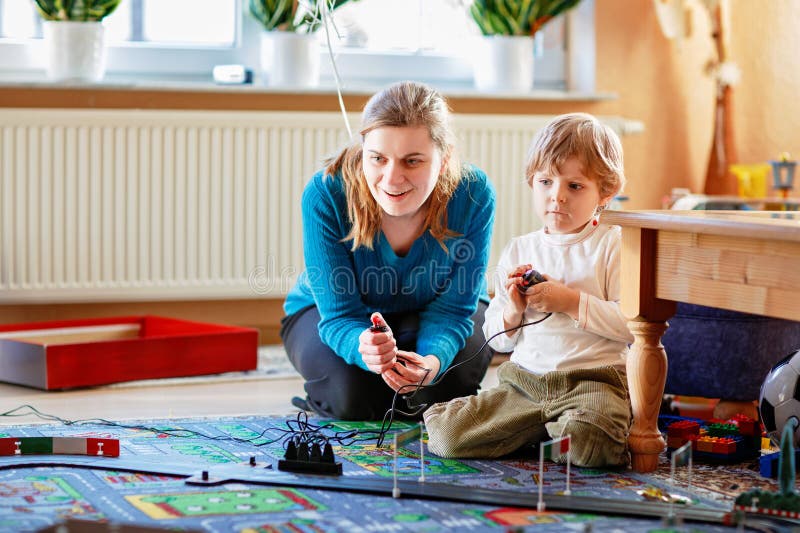 Mor och son leker med tävlingsbilar på racerbak inomhus med bilar. Glad liten förskolepojke och ung kvinna arkivfoton