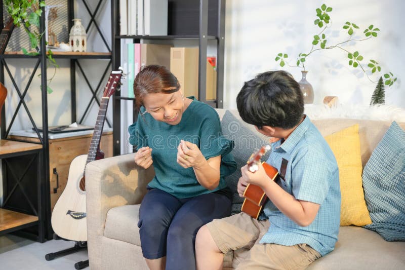 Mor och son som gillar musik tillsammans på hempojken som spelar Ukulele för sin Cheerful Grandma fotografering för bildbyråer