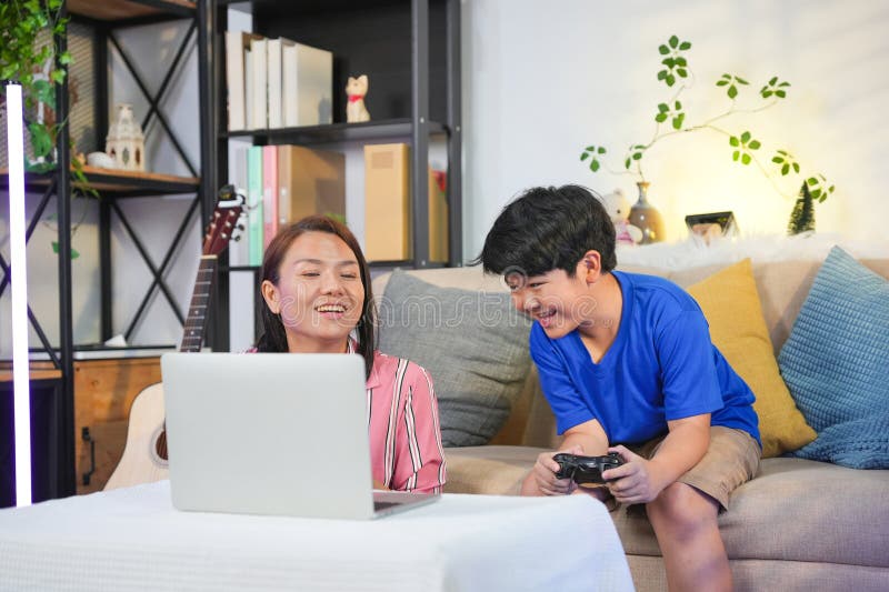 Mor och son som gillar onlinespel tillsammans med unga asiatiska barn som spelar videospel med förälder och son som binder sig öve arkivbild