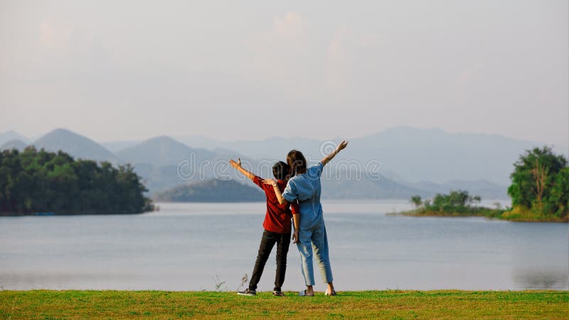 Mor och son som står bredvid stor sjö och ser bergsvyn i bakgrunden. Tanken på familjeturister reser tillsammans till