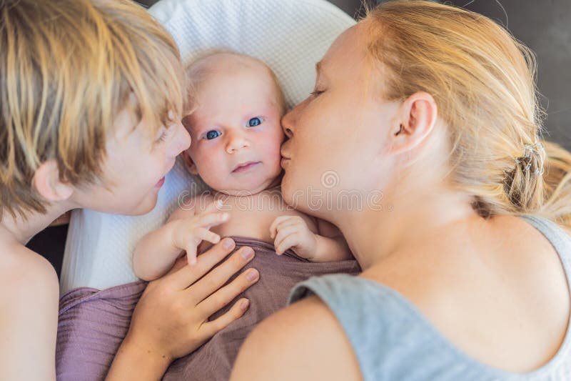 Mor och äldre son beundrar sitt nyfödda barn i ett mysigt spädbarn. Familjeband och syskonkärlek royaltyfri bild