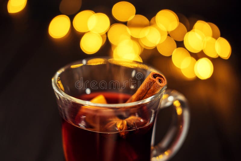 Morceau de plan rapproché de verre de vin chaud avec l'orange et la cannelle sur le fond noir foncé, lumières de Noël, l image libre de droits Morceau de plan rapproché de verre de vin chaud avec l'orange et la cannelle sur le fond noir foncé, lumières de Noël, l image libre de droits