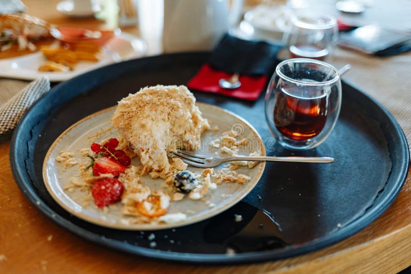 Morceau mordu de gâteau crème fouetté, d'une tasse de thé et d'une cuillère sur un plateau rond noir sur une table dans un café photographie stock libre de droits Morceau mordu de gâteau crème fouetté, d'une tasse de thé et d'une cuillère sur un plateau rond noir sur une table dans un café photographie stock libre de droits