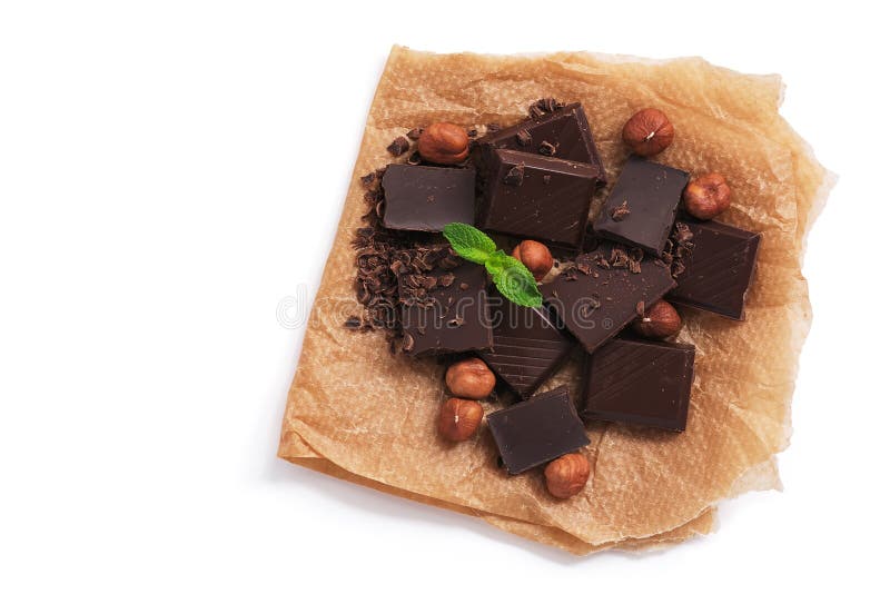 Morceaux de chocolat noir, noisettes et menthe sur papier parchemin, fond blanc, isolés Vue depuis le haut photo stock Morceaux de chocolat noir, noisettes et menthe sur papier parchemin, fond blanc, isolés Vue depuis le haut photo stock