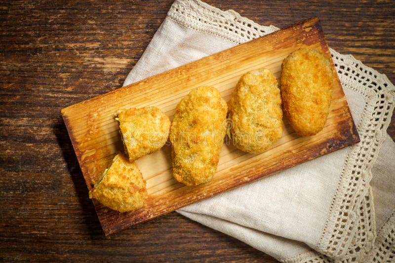 Crispy fried cheddar cheese jalapeno popper bites served on wooden cedar plate with dark moody lighting. Crispy fried cheddar cheese jalapeno popper bites served on wooden cedar plate with dark moody lighting