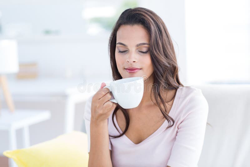 Morena bonita de sorriso que relaxa no sofá e em guardar a caneca foto de stock Morena bonita de sorriso que relaxa no sofá e em guardar a caneca foto de stock