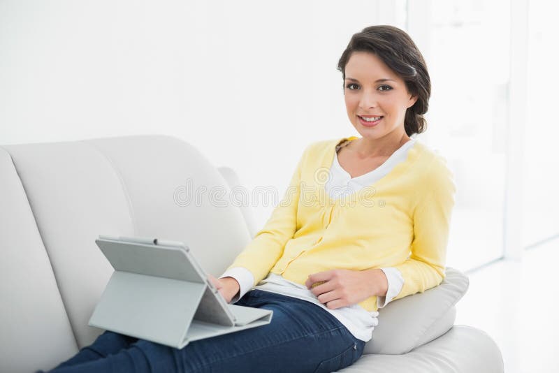 Morena ocasional de sorriso no casaco de lã amarelo usando um PC da tabuleta foto de stock Morena ocasional de sorriso no casaco de lã amarelo usando um PC da tabuleta foto de stock