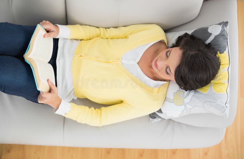 Morena ocasional satisfeita no casaco de lã amarelo que lê um livro imagens de stock royalty free Morena ocasional satisfeita no casaco de lã amarelo que lê um livro imagens de stock royalty free