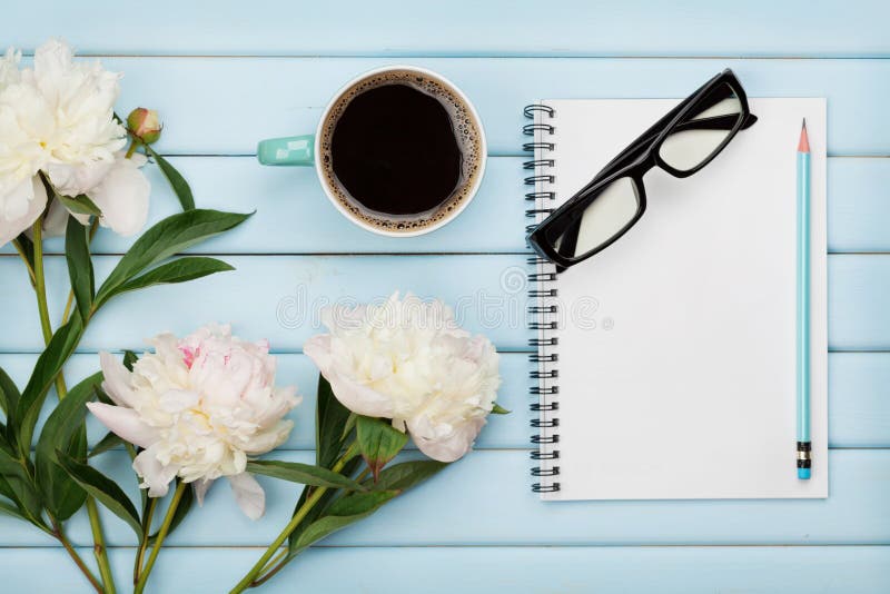 Morning coffee mug, empty notebook, pencil, glasses and white peony flowers on blue wooden table, cozy summer breakfast, top view, flat lay. Morning coffee mug, empty notebook, pencil, glasses and white peony flowers on blue wooden table, cozy summer breakfast, top view, flat lay