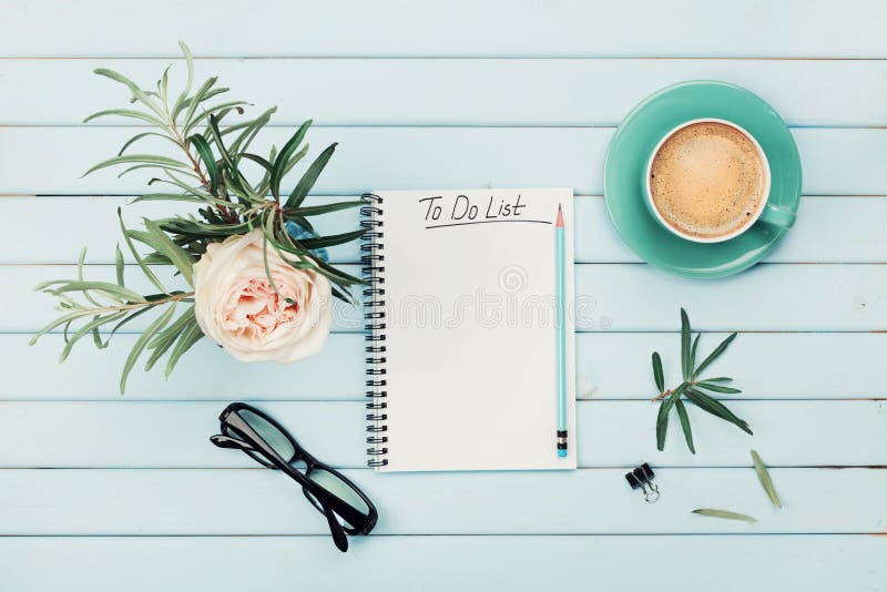 Morning coffee cup, notebook with to do list, pencil, eyeglasses and vintage rose flower in vase on blue rustic table from above. Planning and design concept. Cozy breakfast. Flat lay styling. Morning coffee cup, notebook with to do list, pencil, eyeglasses and vintage rose flower in vase on blue rustic table from above. Planning and design concept. Cozy breakfast. Flat lay styling.
