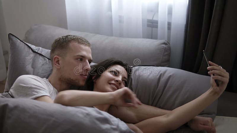 Morgonselfie av gifta paret Lyckliga härliga unga par som ligger på sängen som gör självståenden vid smartphonen man