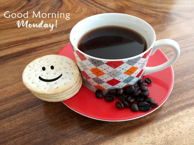 Morning coffee. Cup of black coffee and raw coffee beans with smiling face on cookies and text greeting - Good morning Monday. On natural background of wooden table