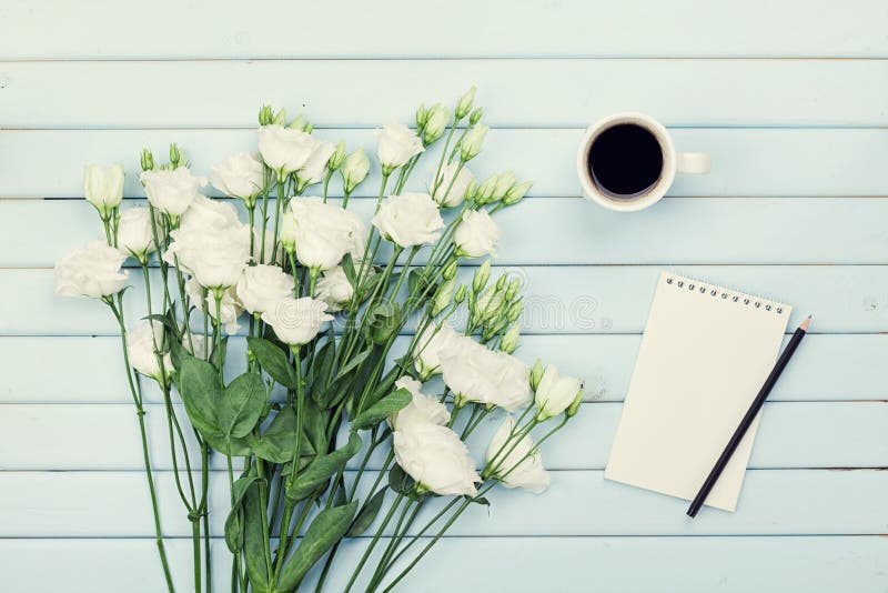 Morning coffee cup, empty paper list, pencil, and bouquet of white flowers eustoma on blue rustic table top view. Flat lay.