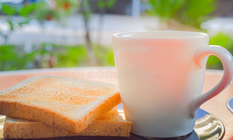 Morning coffee and toasted whole wheat bread on black plate on the red table with smoke over the cup of coffee in the sunshine.