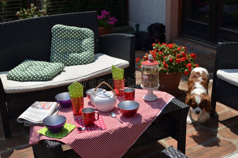 Morning in a Garden. Set of garden furniture with served breakfast and with pets and flowers around stock photos