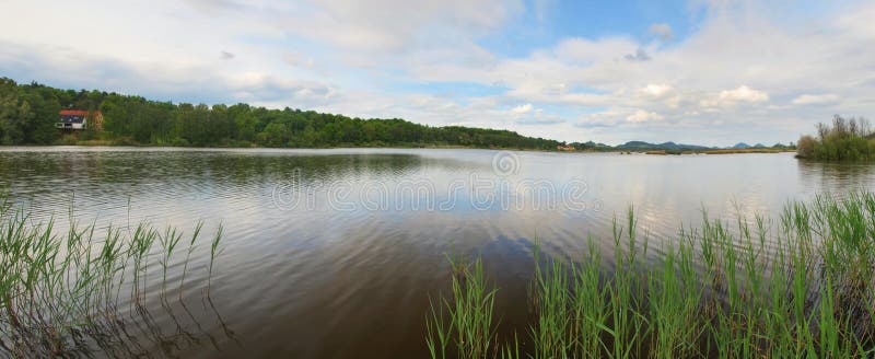 Morning panorama view over lake from fishing place to opposite bank, reflection of sky in the water level.