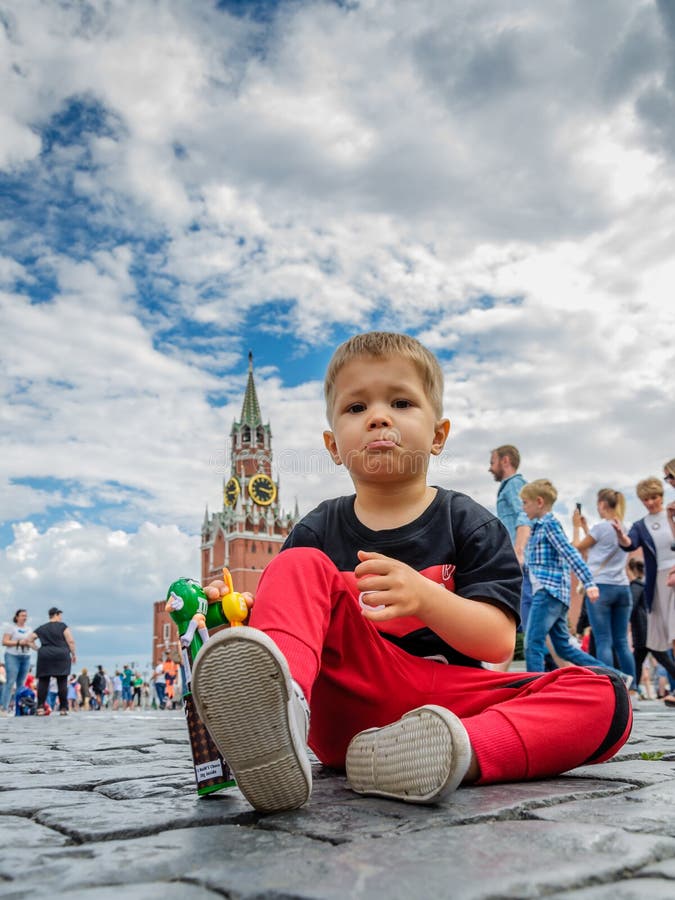 Moscou, Rússia - 7 de julho de 2018: o menino insatisfeito, não feliz senta-se em pedras de pavimentação de quadrado vermelho, em