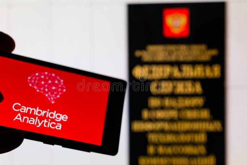 MOSCOW, RUSSIA - MAY 9, 2018: Smartphone in hand with Cambridge Analytica logo infamous after the leakage of personal data from Facebook. Entrance to Roskomnadzor office in background. GDPR concept. MOSCOW, RUSSIA - MAY 9, 2018: Smartphone in hand with Cambridge Analytica logo infamous after the leakage of personal data from Facebook. Entrance to Roskomnadzor office in background. GDPR concept.