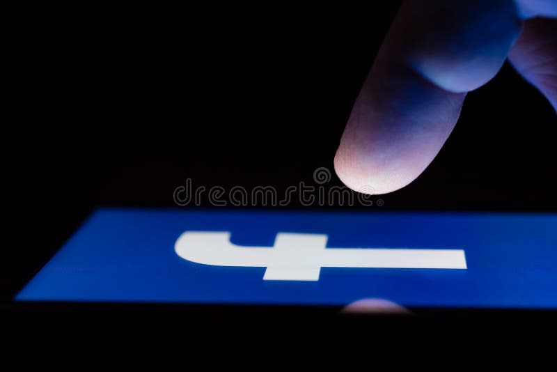 MOSCOW, RUSSIA - May 9, 2018: A smartphone lying on a table in the dark, displaying the logo of the Facebook. The finger above touch screen. The concept of dependence on popular social networks. MOSCOW, RUSSIA - May 9, 2018: A smartphone lying on a table in the dark, displaying the logo of the Facebook. The finger above touch screen. The concept of dependence on popular social networks.