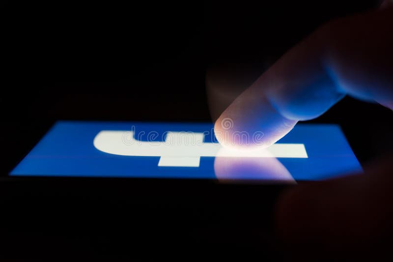 MOSCOW, RUSSIA - May 9, 2018: A smartphone lying on a table in the dark, displaying the logo of the Facebook. The finger above touch screen. The concept of dependence on popular social networks. MOSCOW, RUSSIA - May 9, 2018: A smartphone lying on a table in the dark, displaying the logo of the Facebook. The finger above touch screen. The concept of dependence on popular social networks.