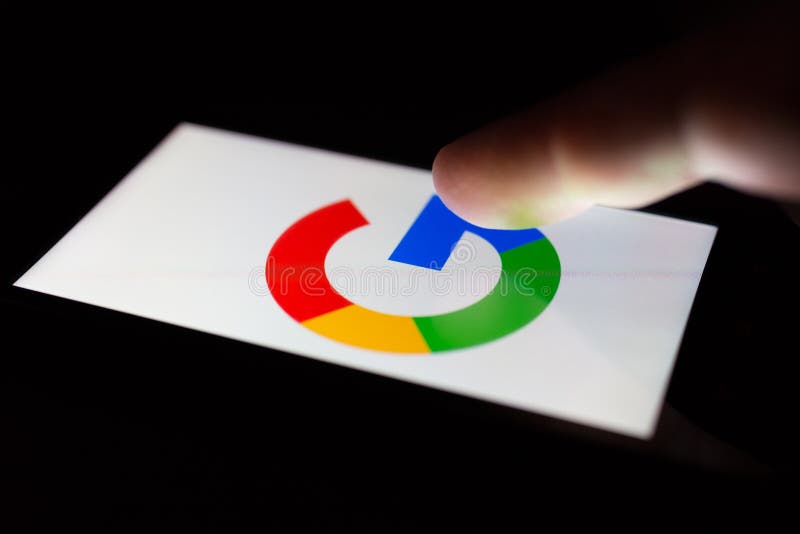 MOSCOW, RUSSIA - May 9, 2018: A smartphone lying on a table in the dark, displaying the logo of the Google. The finger above touch screen. The concept of dependence on Internet surfing. MOSCOW, RUSSIA - May 9, 2018: A smartphone lying on a table in the dark, displaying the logo of the Google. The finger above touch screen. The concept of dependence on Internet surfing.