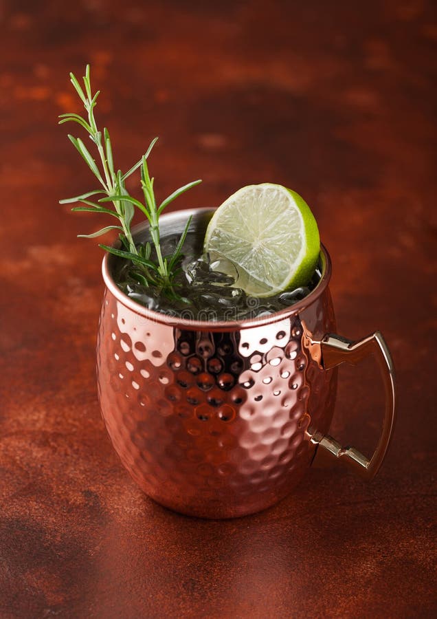 Moscow Mule Cocktail in a Copper Mug with Lime and Rosemary on Brown