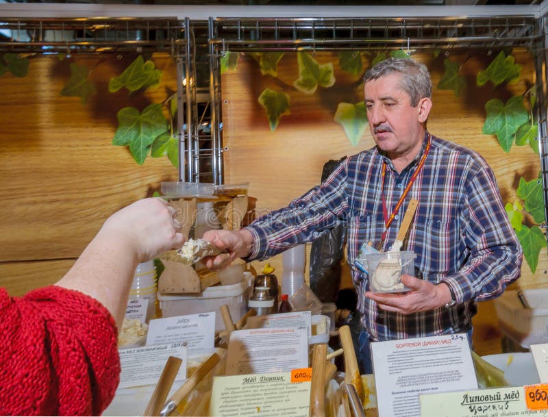 Moscow, Russia - February 25, 2017: Salesman at the fair offers to try home produced honey from his showcase. Moscow, Russia - February 25, 2017: Salesman at the royalty free stock images Moscow, Russia - February 25, 2017: Salesman at the fair offers to try home produced honey from his showcase. Moscow, Russia - February 25, 2017: Salesman at the royalty free stock images