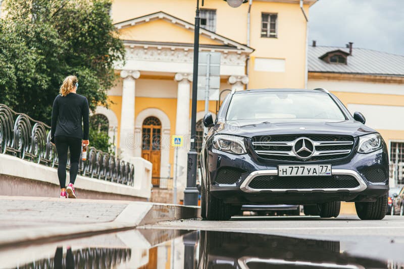 Moscow, Russia - JULY 7, 2017: A young girl with a sporty figure walks past a deep blue Mercedes Benz GLC 250 4Matic