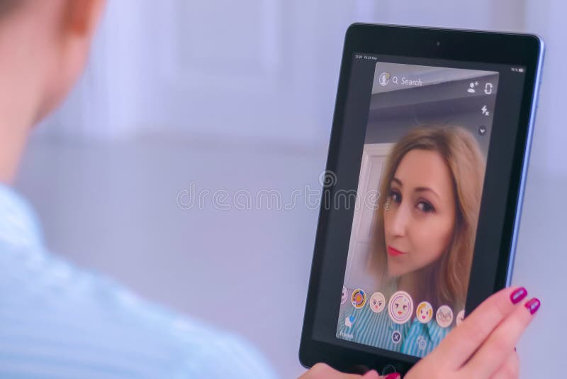 Woman using Snapchat multimedia messaging app with face mask on tablet